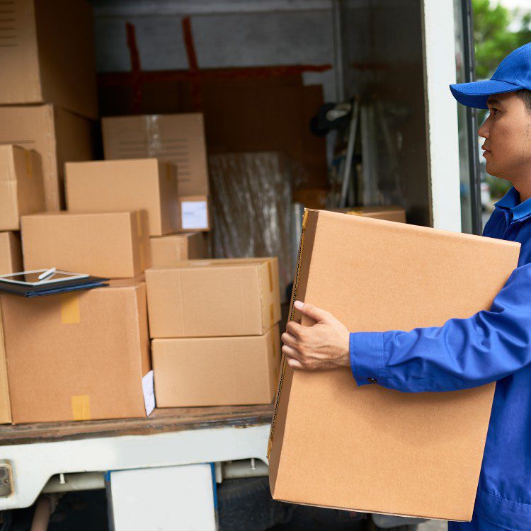 Delivery worker in blue uniform loading cardboard boxes into a truck