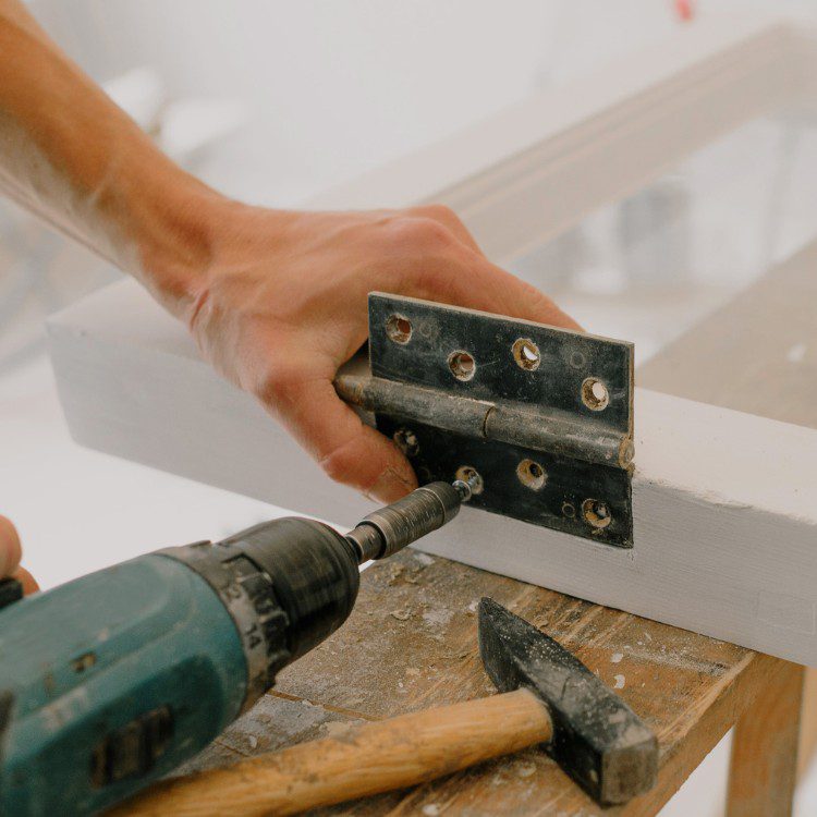 Hand drilling metal hinge into wooden surface with power drill