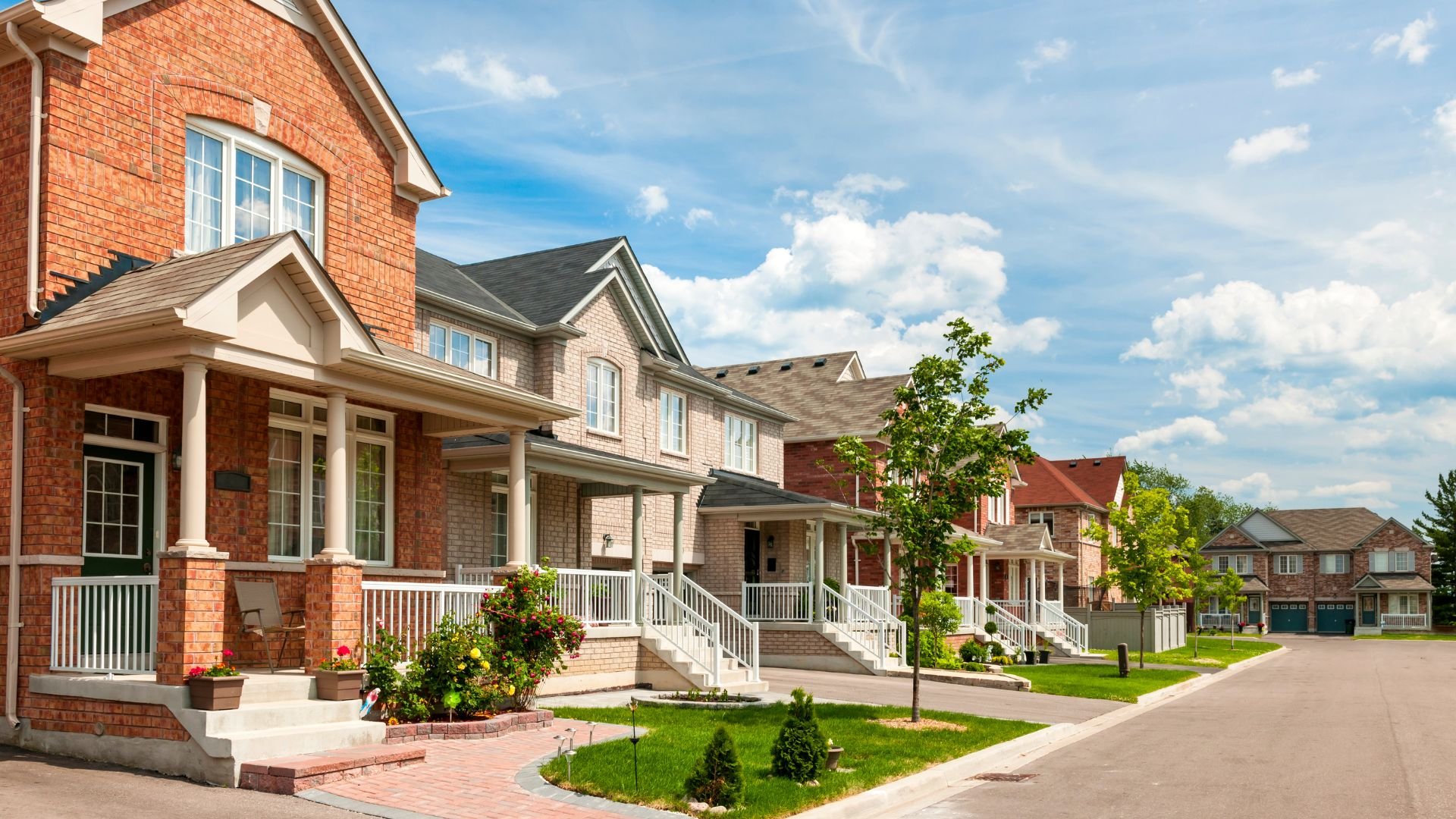 Suburban street with new brick houses and manicured lawns on sunny day